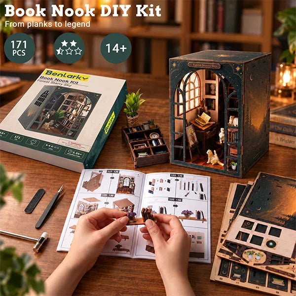 A DIY book nook kit shown on a wooden table with a person's hands assembling pieces from an instruction booklet. The kit includes a decorative wooden nook structure with a lit arched window, the product box, loose components, and accessories.