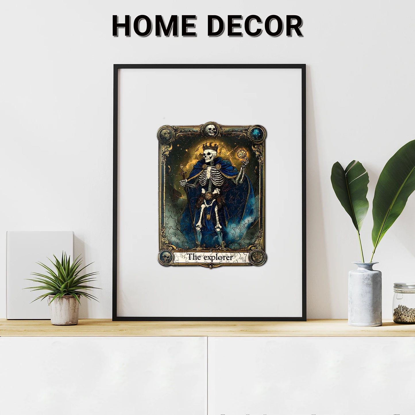 A framed art print inspired by benlarkytoys’ Wooden Puzzles for Adults—200 uniquely irregular Skull Explorer Tarot-shaped pieces—hangs above a white cabinet with plants, capturing the creative intrigue of an adult jigsaw puzzle. HOME DECOR appears above.