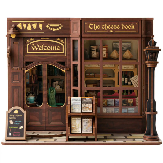 A miniature wooden diorama model of 'The Cheese Book' shop from Harry Potter, featuring detailed brown wood grain, gold lettering, miniature shelves, and a street lamp on a white background.